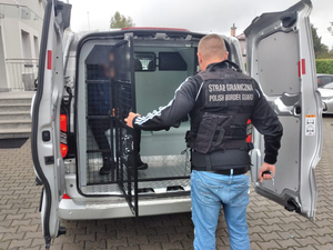  Funkcjonariusz SG zamykający kratę w samochodzie. W środku osoba zatrzymana.