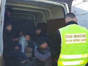 Funkcjonariusz SG stoi przy samochodzie dostawczym z nielegalnymi migrantami 