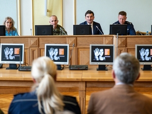  Ujęcie z widowni na prowadzących spotkanie. Przed nimi ekrany komputerów wyświetlające młodą kobietę z wyciągniętą dłonią na znak &amp;quot;stop&amp;quot;