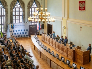  Duża sala. Licznie zgromadzeni słuchacze podczas wykładu. Ścianka reklamowa z napisem Miasto Żywiec.