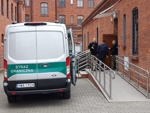  Zdjęcie poglądowe. Samochód SG, Funkcjonariusze prowadzą osobę zatrzymaną do budynku