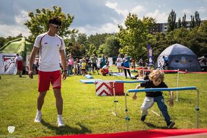  Tor przeszkód. Młody mężczyzna w białych okularach spogląda na dziecko przechodzące pod płotkami.