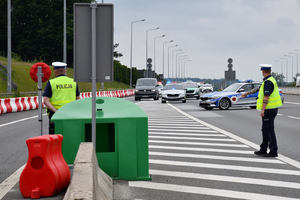  Policjant tarczką stop wskazuje miejsce do zatrzymania. Po bokach ściganego pojazdu jada samochody Policji i Straży Granicznej