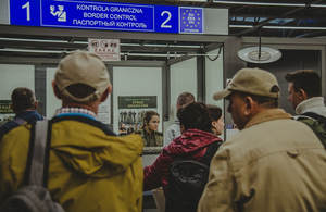  Podróżni stojący przy okienku do odprawy granicznej. W środku siedzi funkcjonariuszka SG.