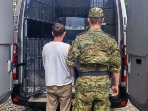  Funkcjonariusz SG i osoba zatrzymana stoją przy zamkniętej kracie samochodu do przewozu osób.