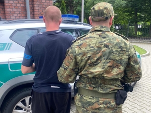  Funkcjonariusz SG i osoba zatrzymana stoją przy samochodzie Straży Granicznej.