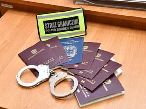  na stole leżą kajdanki, paszporty i emblemat z napisem Straż Graniczna