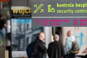 Zdjęcie ilustracyjne. Lotnisko, rozmazane osoby, częściowe napisy: kontrola bezpieczeństwa.