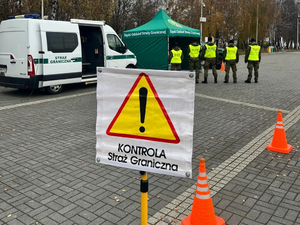 Samochód i namiot Straży granicznej, 5 funkcjonariuszy stojących tyłem, na pierwszym planie znak ostrzegawczy a pod nim napis "Kontrola Straż Graniczna".