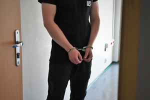  Osoba zatrzymana,ubrana na czarno, na rękach ma założone kajdanki