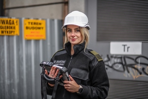  Młoda funkcjonariuszka SG pozująca z tabletem. Na głowie ma biały kask.