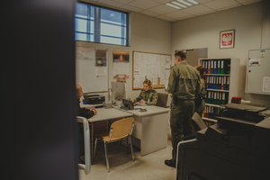  Pomieszczenie, biurka, przy 2 z nich siedzą funkcjonariusze, kolejna dwójka funkcjonariuszy stoi obok.