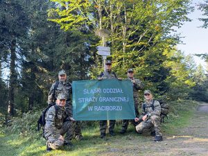  Funkcjonariusze trzymający flagę z napisem: Śląski Oddział Straży Granicznej w Raciborzu.