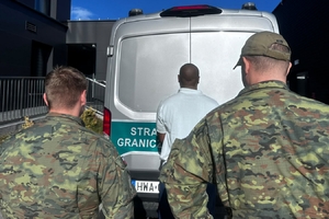  2 Strażników Granicznych. Przed nimi w białej koszulce stoi osoba zatrzymana. Jest noc.